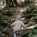 boy in brown sweater and blue denim jeans walking on green grass during daytime