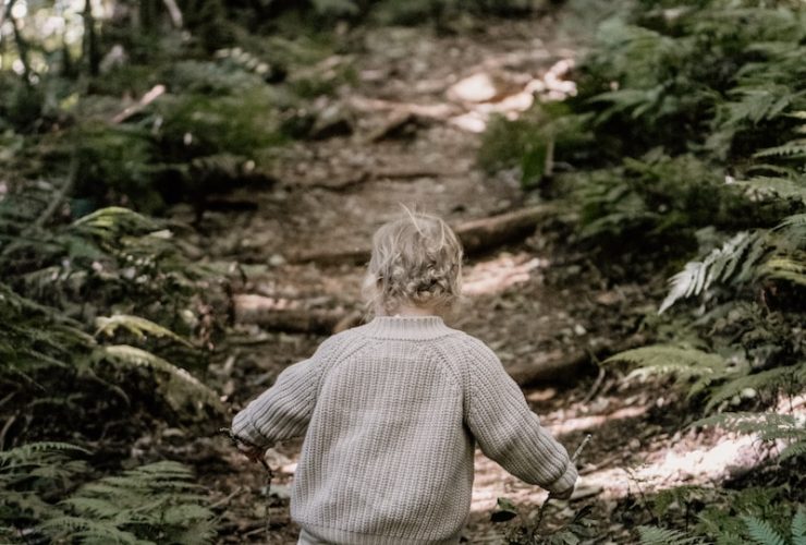 boy in brown sweater and blue denim jeans walking on green grass during daytime