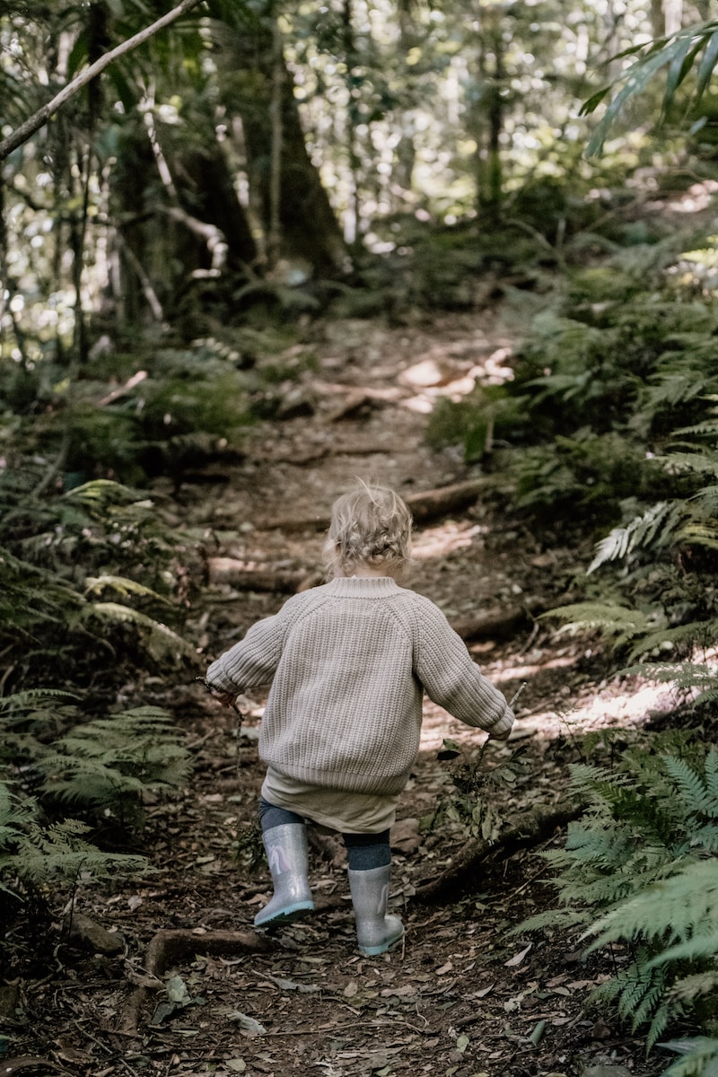 boy in brown sweater and blue denim jeans walking on green grass during daytime