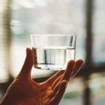 person holding clear glass cup with half-filled water