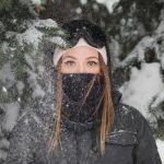 woman with mask standing beside pine tree covered with snow