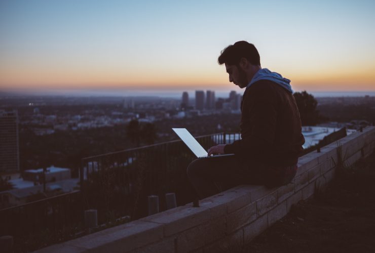 man sitting on concrete brick with opened laptop on his lap