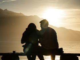 silhouette of man and woman sitting on bench near body of water during sunset