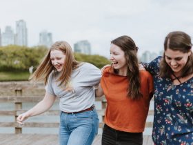 three women walking on brown wooden dock near high rise building during daytime