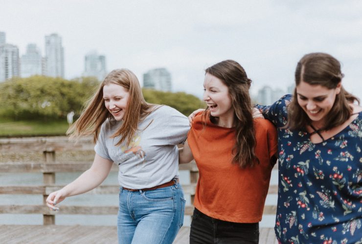 three women walking on brown wooden dock near high rise building during daytime