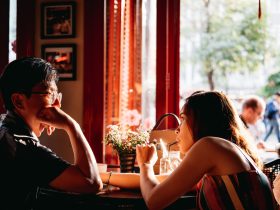 man wearing black collared top sitting on chair in front of table and woman wearing multicolored top