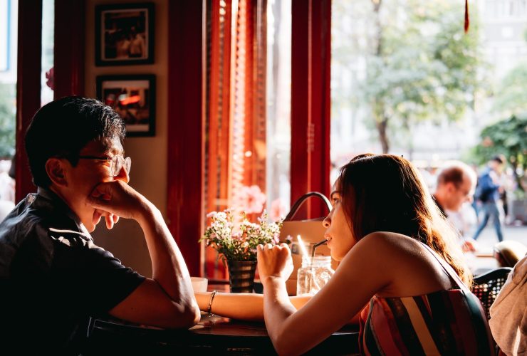 man wearing black collared top sitting on chair in front of table and woman wearing multicolored top