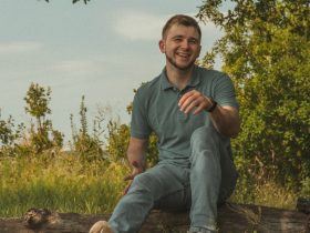 man in green polo shirt and blue denim jeans sitting on brown wooden log during daytime