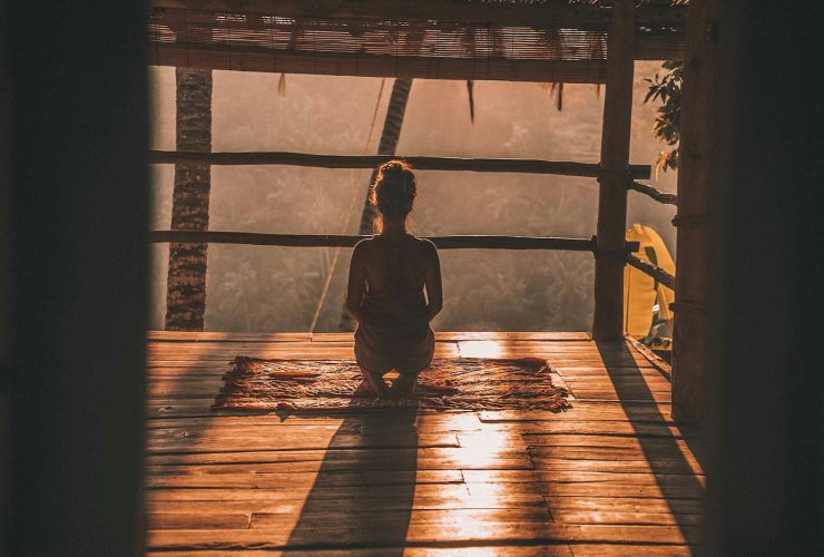 woman meditating on floor with overlooking view of trees