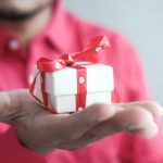 a man holding a white gift box with a red ribbon