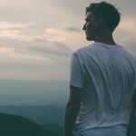 man standing facing mountains during sunset