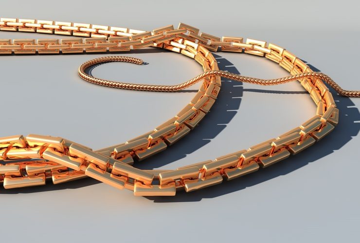 Gouden zomerse sieraden zoals schakelkettingen en enkelbandjes op een strandhanddoek