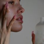 A person applying serum to their cheek with long pink nails
