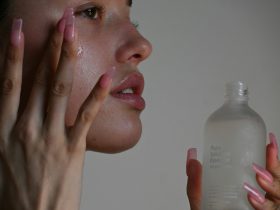 A person applying serum to their cheek with long pink nails