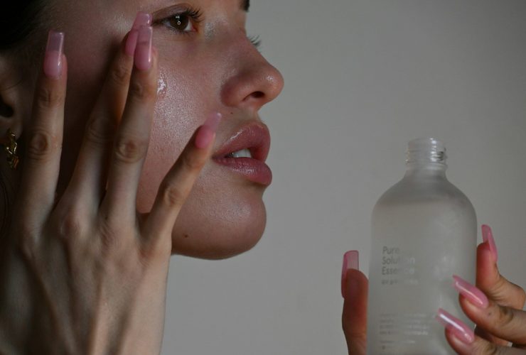 A person applying serum to their cheek with long pink nails